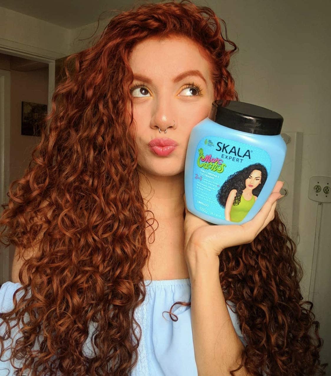 A person with curly red hair holding a jar of SKALA Expert Corn Cachos hair product.
